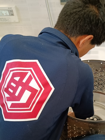仙台市で洗濯機クリーニング作業中の様子。洗濯槽の内部を丁寧に洗浄しているスタッフの背中が写っている写真。